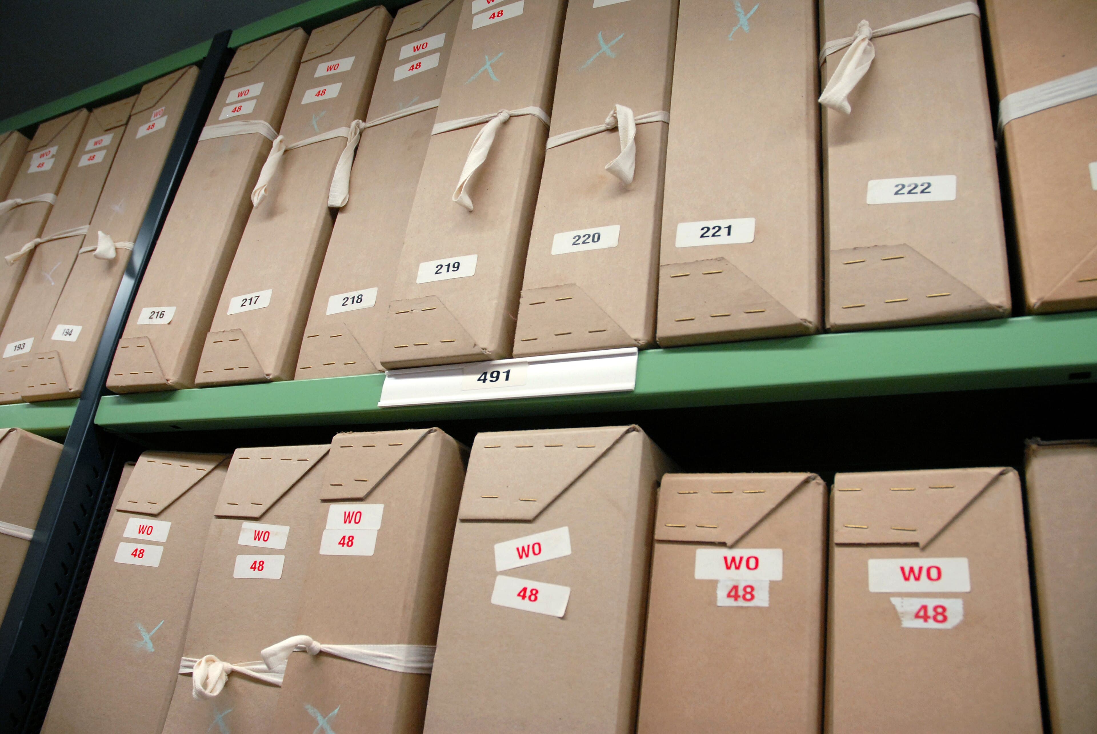 Rows of numbered document boxes tied with tape, on metal shelving in an archive repository