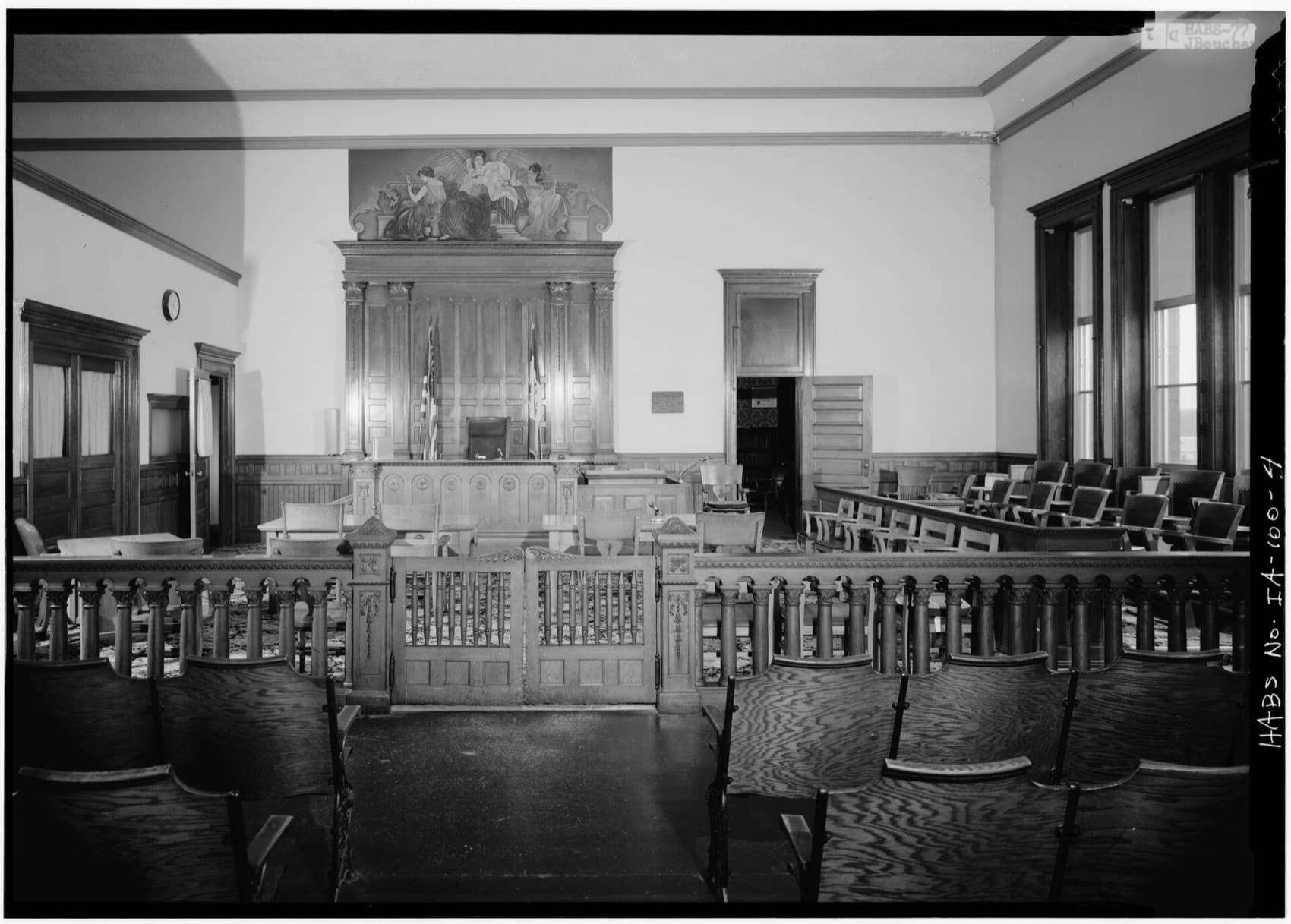 An empty courtroom in black-and-white archive photography: the bench, a wooden rail with a gate, the jury box to the right and public benches in front